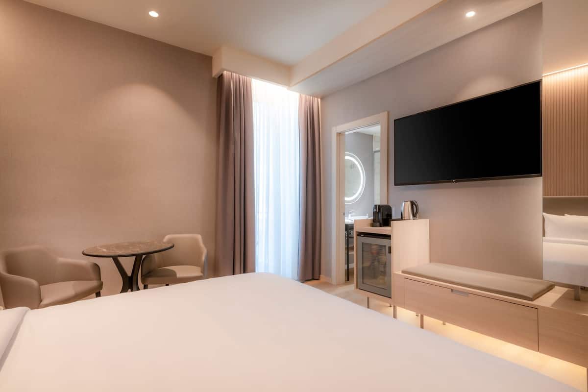Una habitación de hotel moderna con una cama grande, un escritorio, una silla, una mesita y un televisor.
