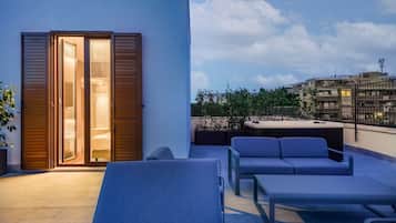Une terrasse sur le toit avec une porte-fenêtre coulissante donnant accès à une chambre, un espace de détente extérieur avec des coussins et une vue sur le paysage urbain.