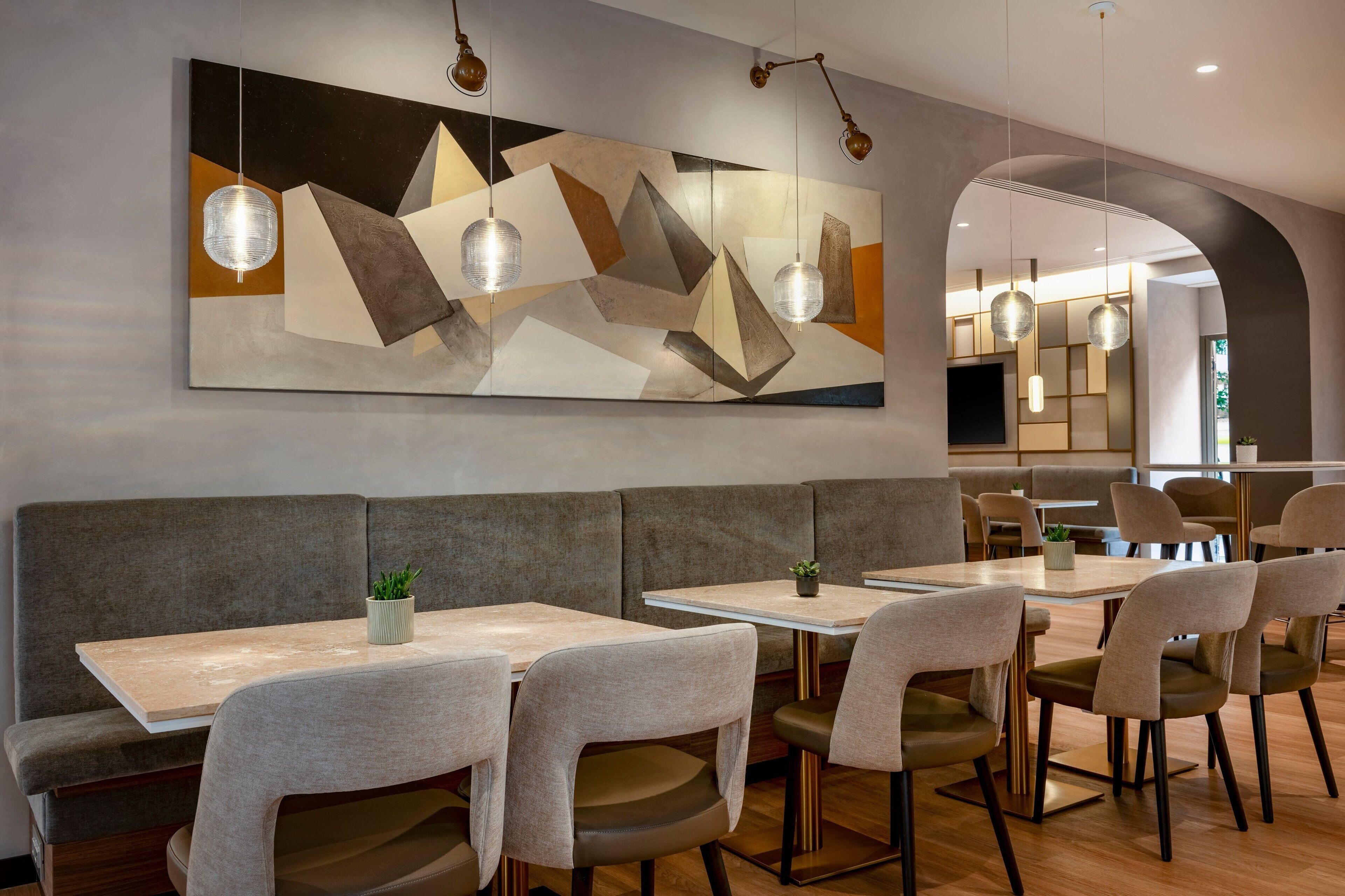 A modern restaurant interior with a large abstract painting, cushioned seating, and pendant lighting.