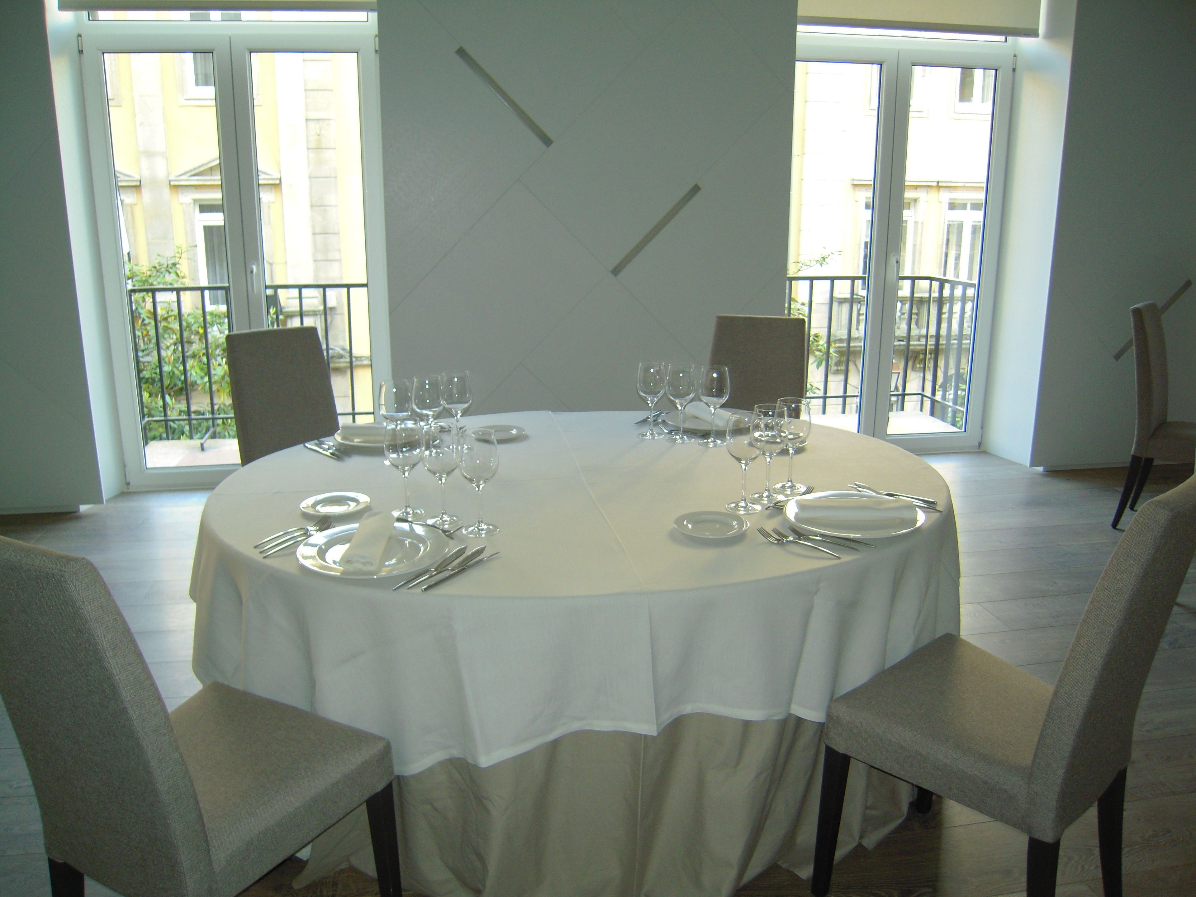 A dining table set for six with white tablecloth, plates, cutlery, and wine glasses.
