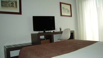 Ein Hotelzimmer mit einem Bett, einem Schreibtisch mit Fernseher und zwei gerahmten Bildern an der Wand.