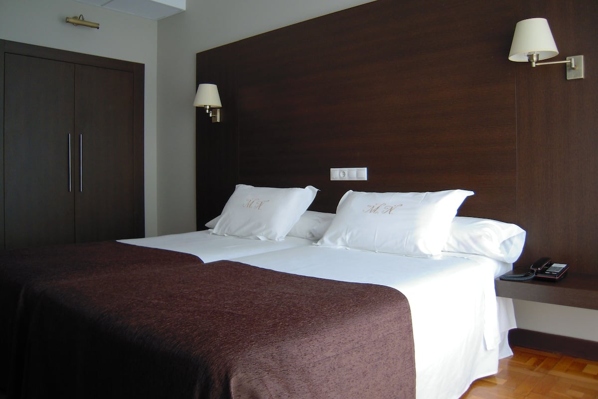 A hotel room with a large bed, two bedside lamps, a wooden headboard, and a wardrobe.