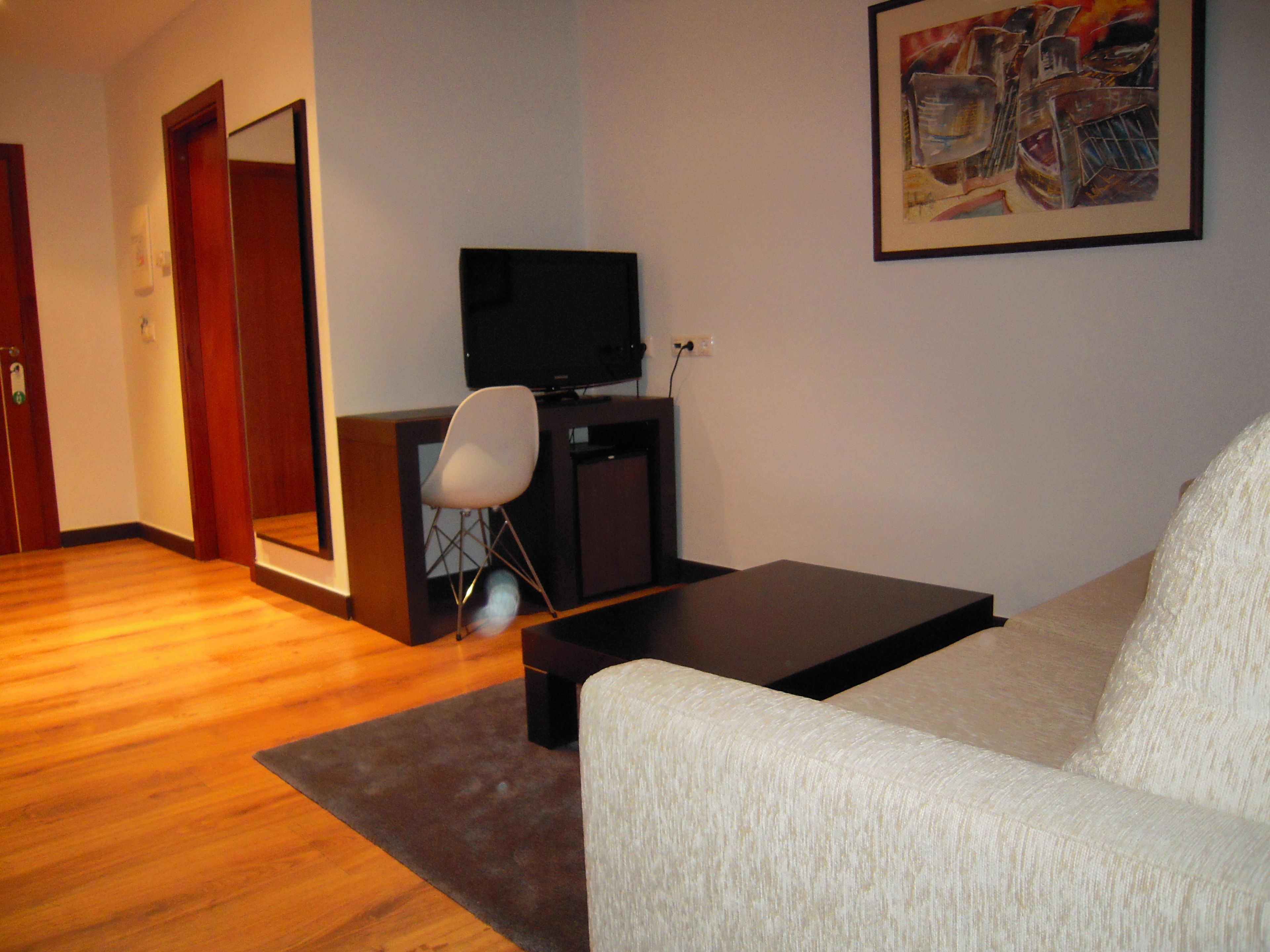 A living room with a sofa, a television, a chair, and a painting on the wall.
