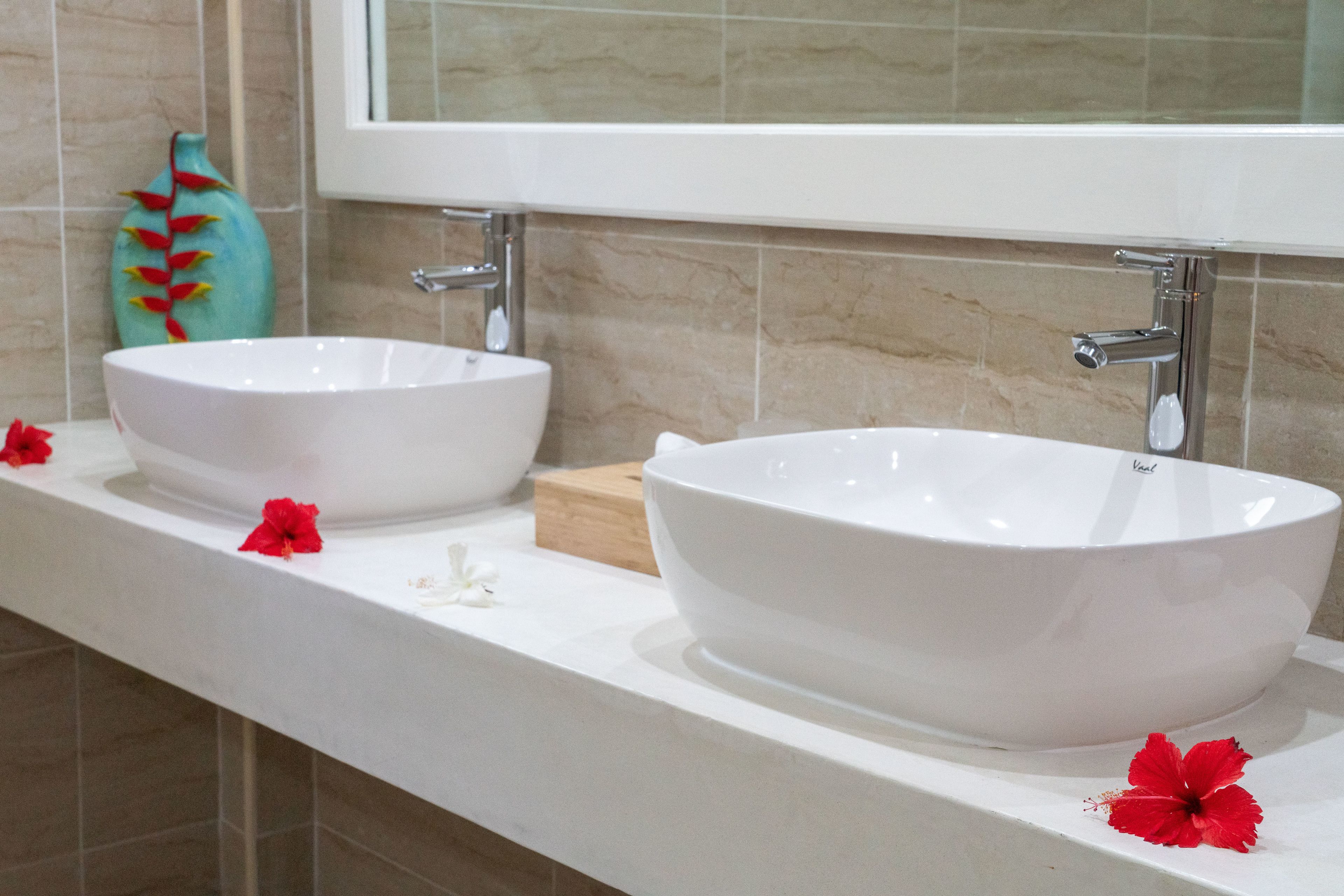 A bathroom with two white vessel sinks, a wooden soap dish, and a decorative vase.