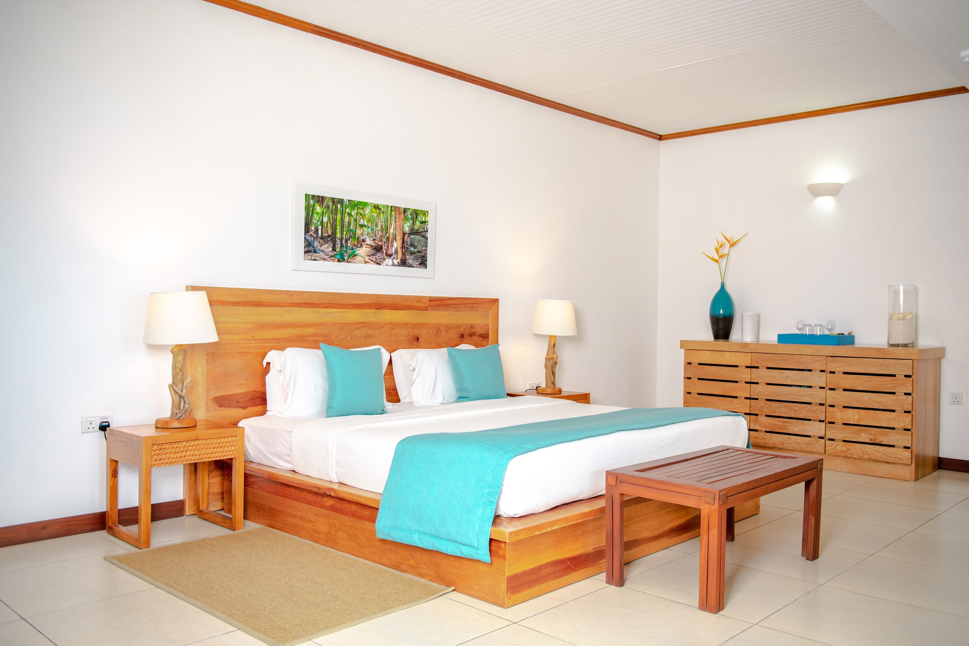 A bedroom with a wooden bed, two bedside tables, a nightstand, a wooden bench, a dresser, and a wall-mounted lamp.