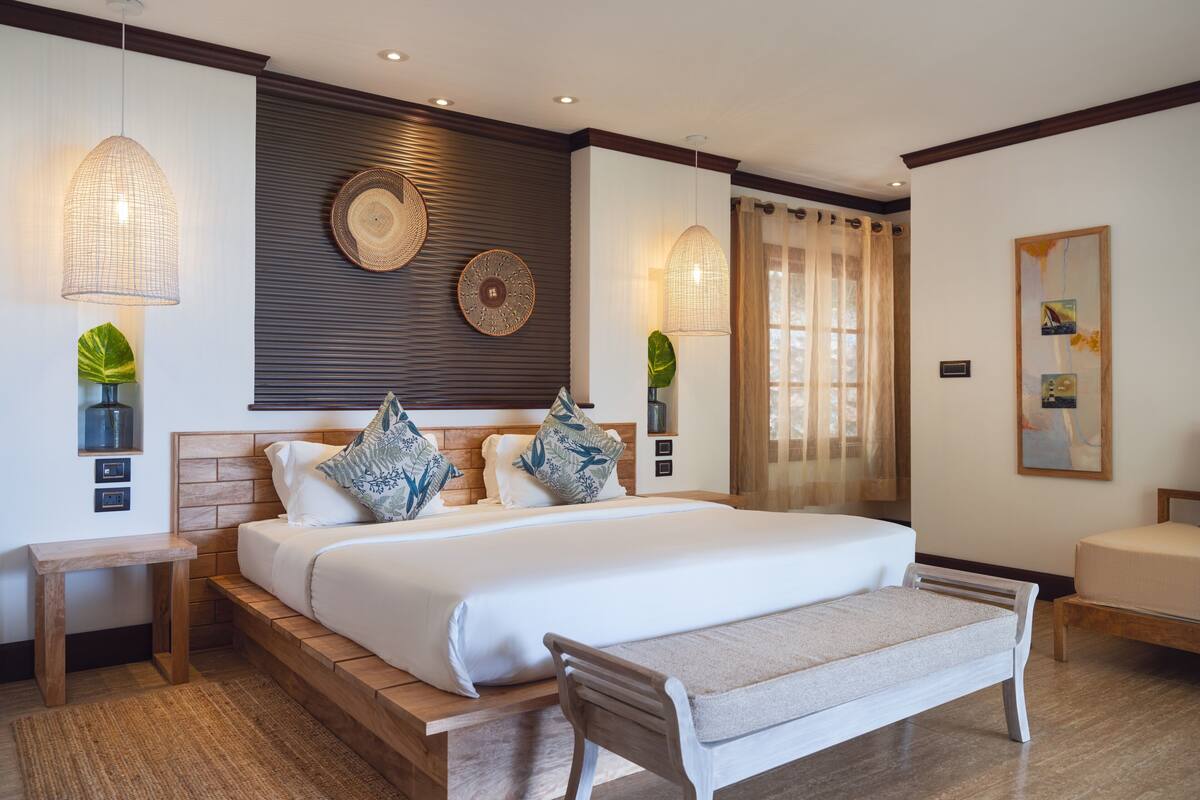 A modern hotel room with a large bed, wooden headboard, bedside tables, and a bench.