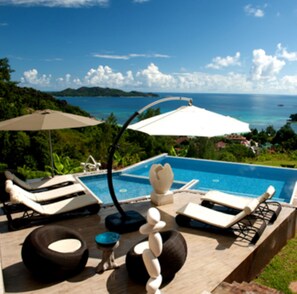 A poolside area with lounge chairs, a pool, and a view of the sea. - Le Duc de Praslin (Praslin Island)