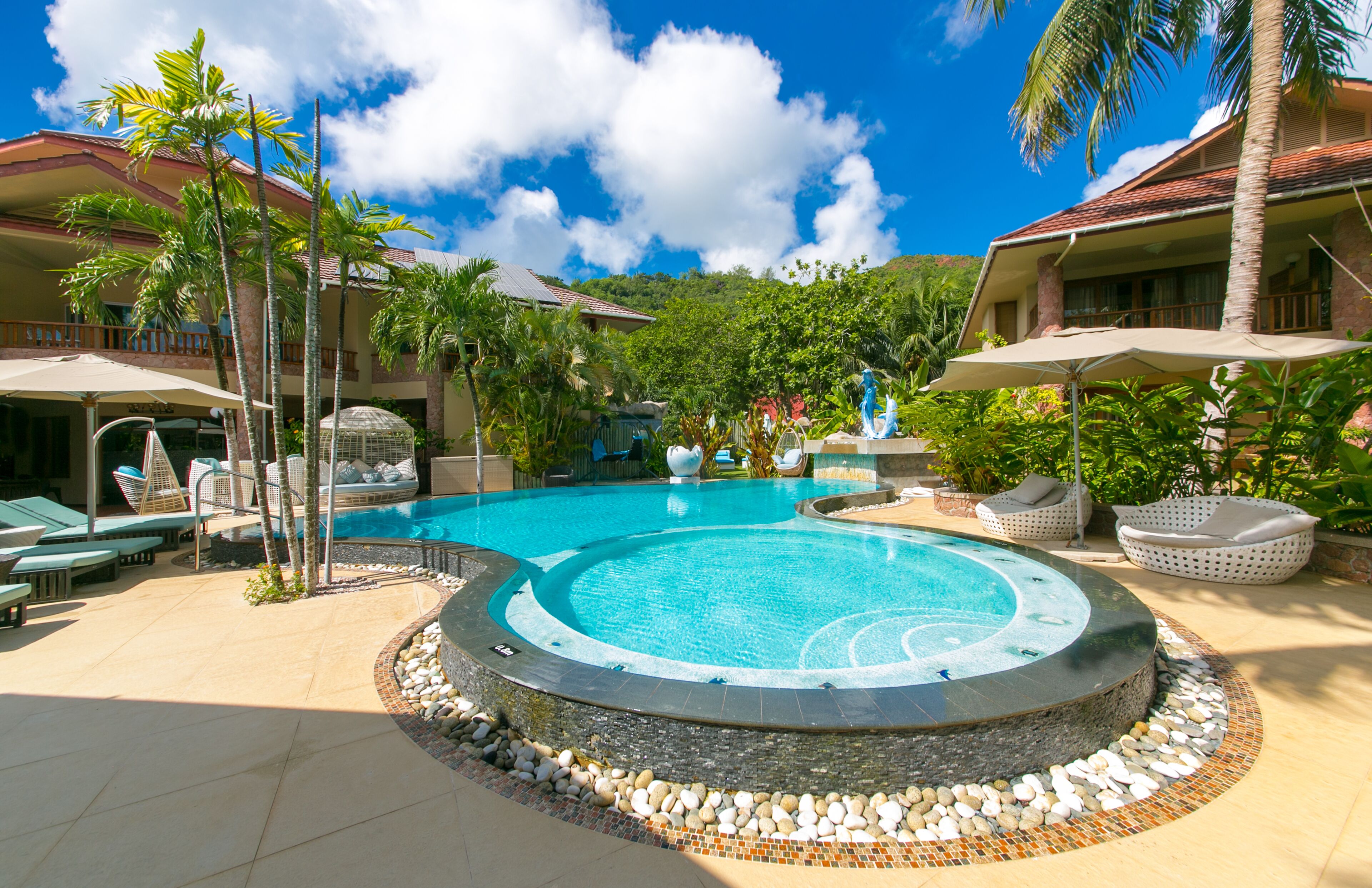 A resort pool area with lounge chairs, palm trees, and a hot tub.
