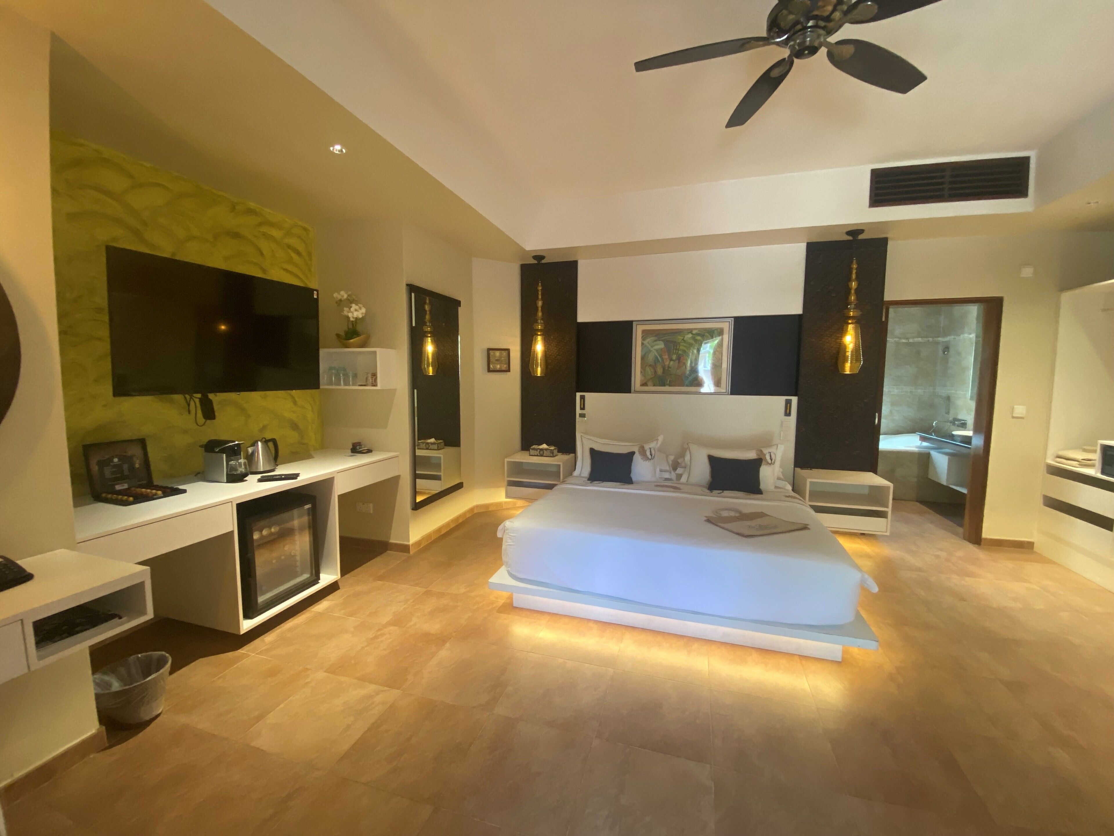 A modern bedroom with a large bed, a desk, a TV, and a ceiling fan.