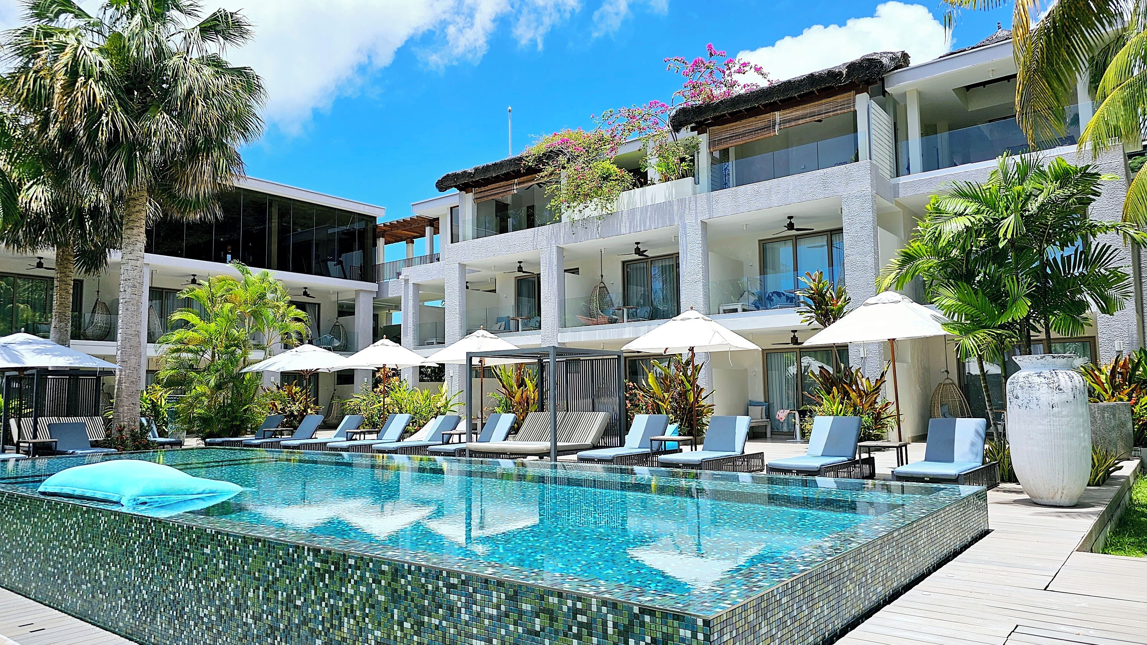 A modern hotel with a swimming pool, sun loungers, and umbrellas.