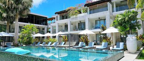 A modern hotel with a swimming pool, sun loungers, and umbrellas.