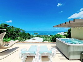 A rooftop terrace with a hot tub, lounge chairs, and a view of the ocean.