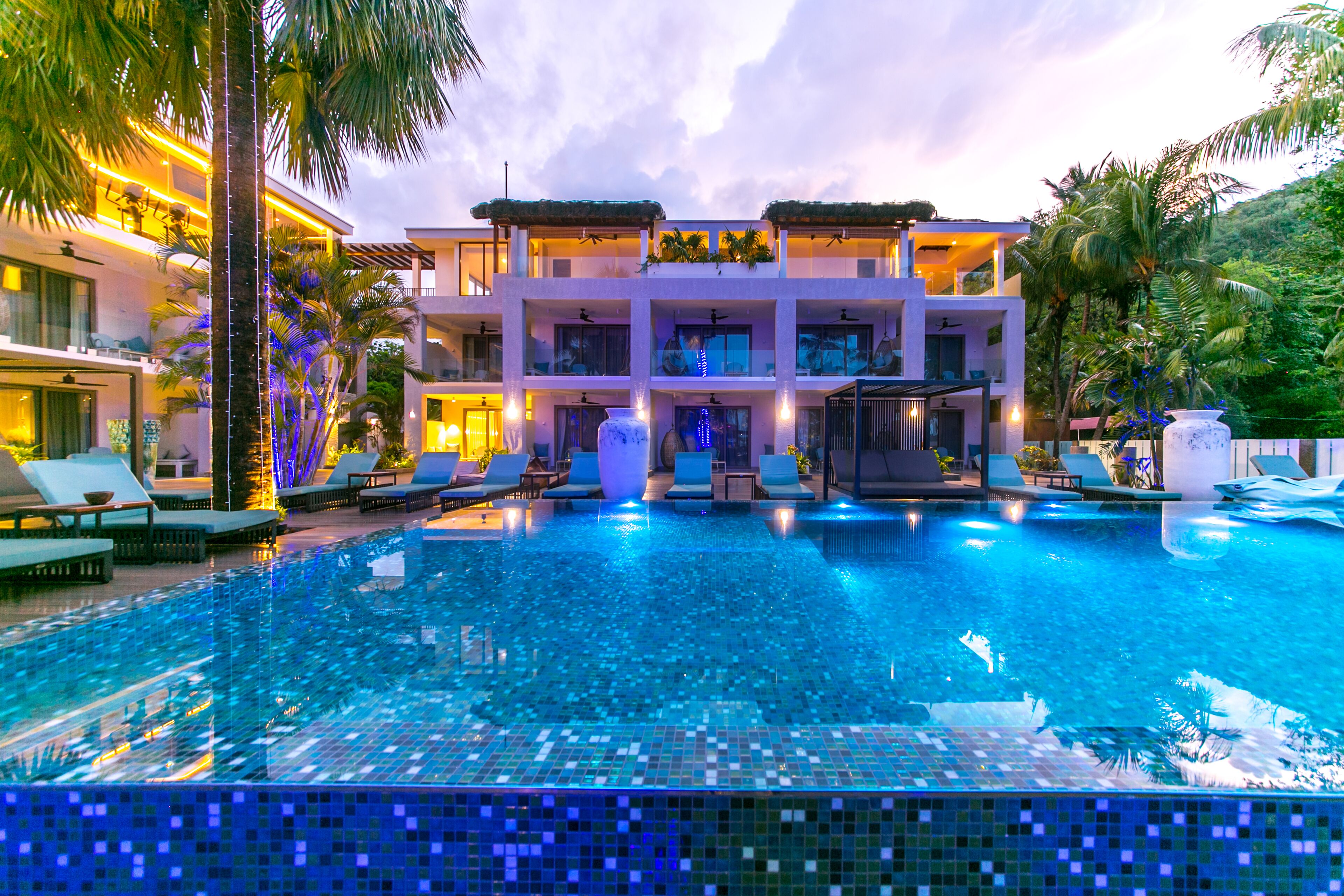 Un hôtel à plusieurs étages doté d’une grande piscine, de palmiers et de chaises longues.