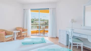 Habitación de hotel con balcón, escritorio, dos sillas de mimbre, cama y una mesita.