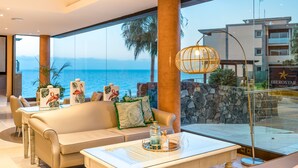 A modern hotel room with a large window offering a view of the sea, a sofa, a coffee table with decorative items, and a tropical-themed decor. - Iberostar Waves Playa Gaviotas -All Inclusive (Pajara)