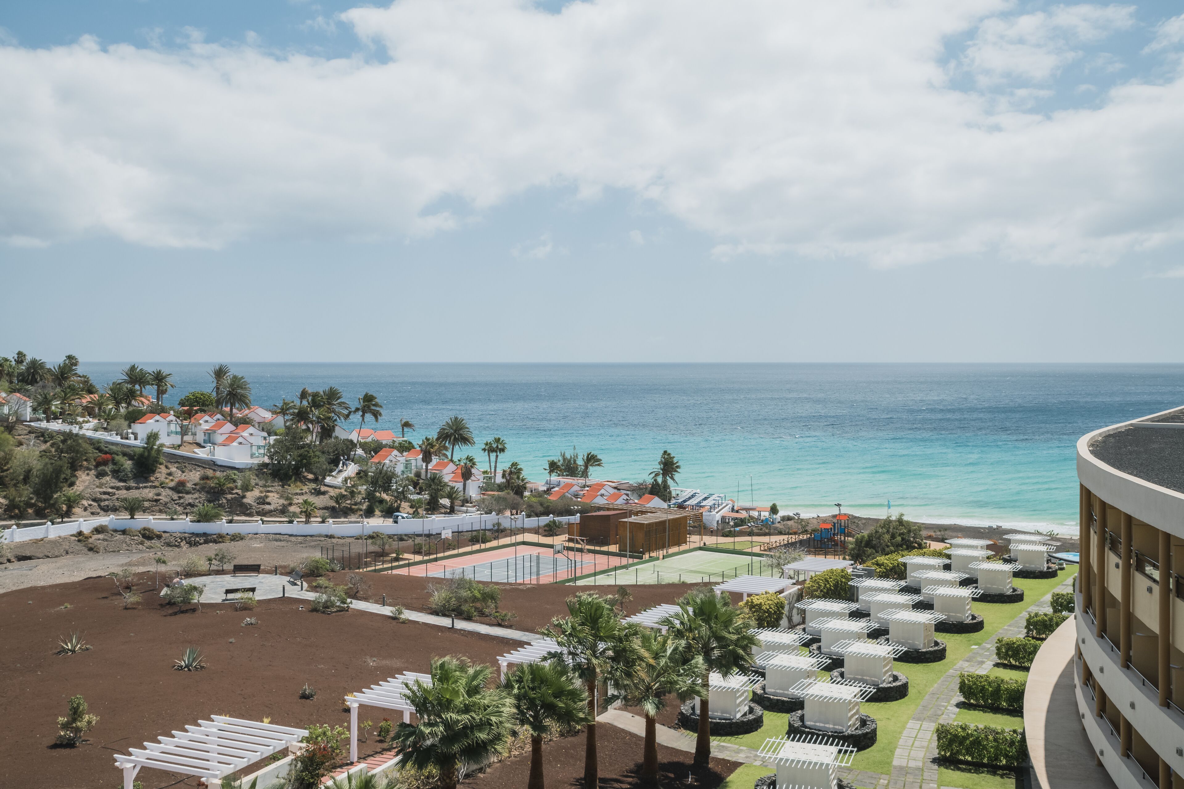 A resort with a view of the ocean, outdoor seating areas, and a tennis court.