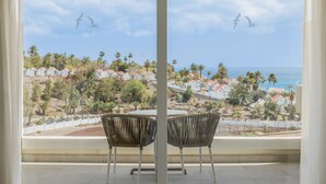 A balcony with two wicker chairs and a table, overlooking a coastal area with houses and palm trees. - Iberostar Waves Playa Gaviotas -All Inclusive (Pajara)