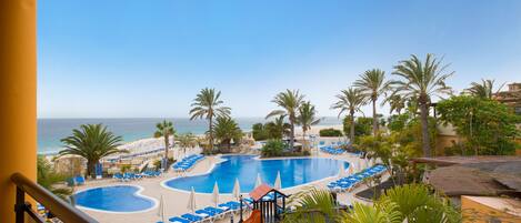 A resort pool area with multiple pools, lounge chairs, and palm trees.
