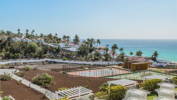 Un quartier résidentiel situé sur la côte, avec des maisons, un court de tennis et une vue sur la mer.