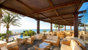 A covered outdoor seating area with wicker furniture, a glass table, and a view of the ocean. - Iberostar Waves Playa Gaviotas -All Inclusive (Pajara)