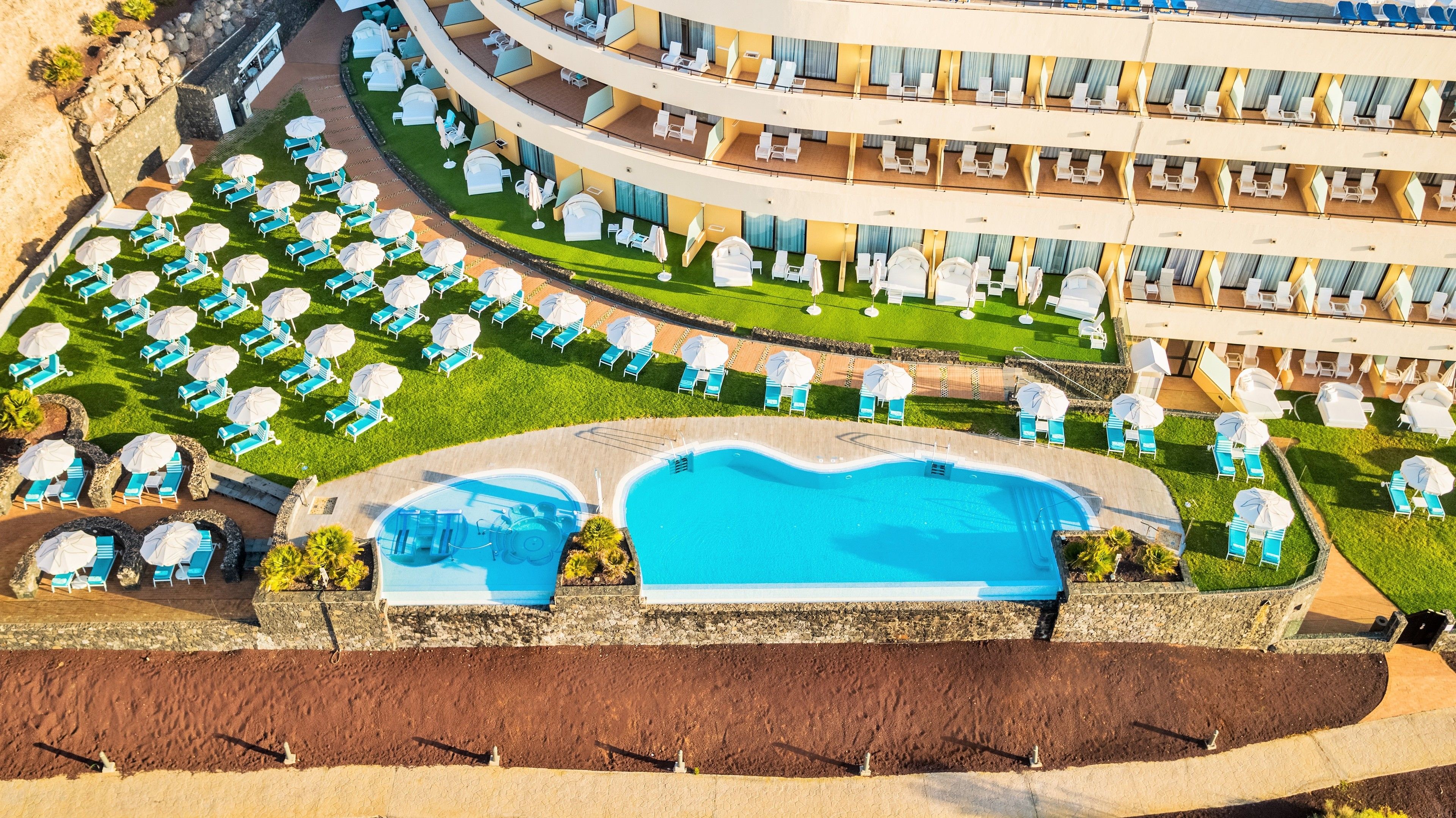 A resort with a large swimming pool, multiple lounge areas with umbrellas, and a multi-level building with balconies.