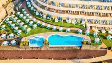 A resort with a large swimming pool, multiple lounge areas with umbrellas, and a multi-level building with balconies.