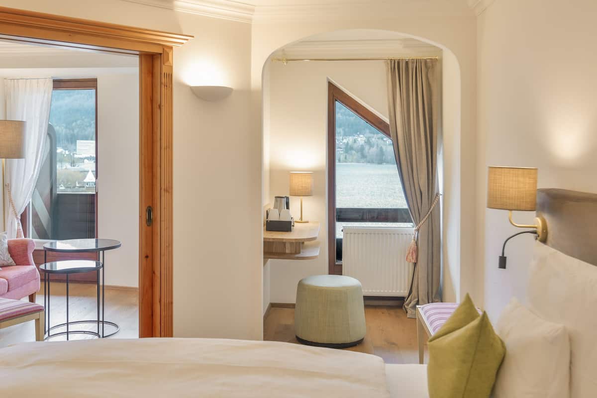 Une chambre d’hôtel avec un lit, une petite table, une chaise, une fenêtre donnant sur un paysage agréable et une lampe.