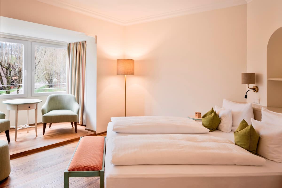 Une chambre d’hôtel avec deux lits, un bureau, une chaise, une lampe et une vue sur les arbres par la fenêtre.