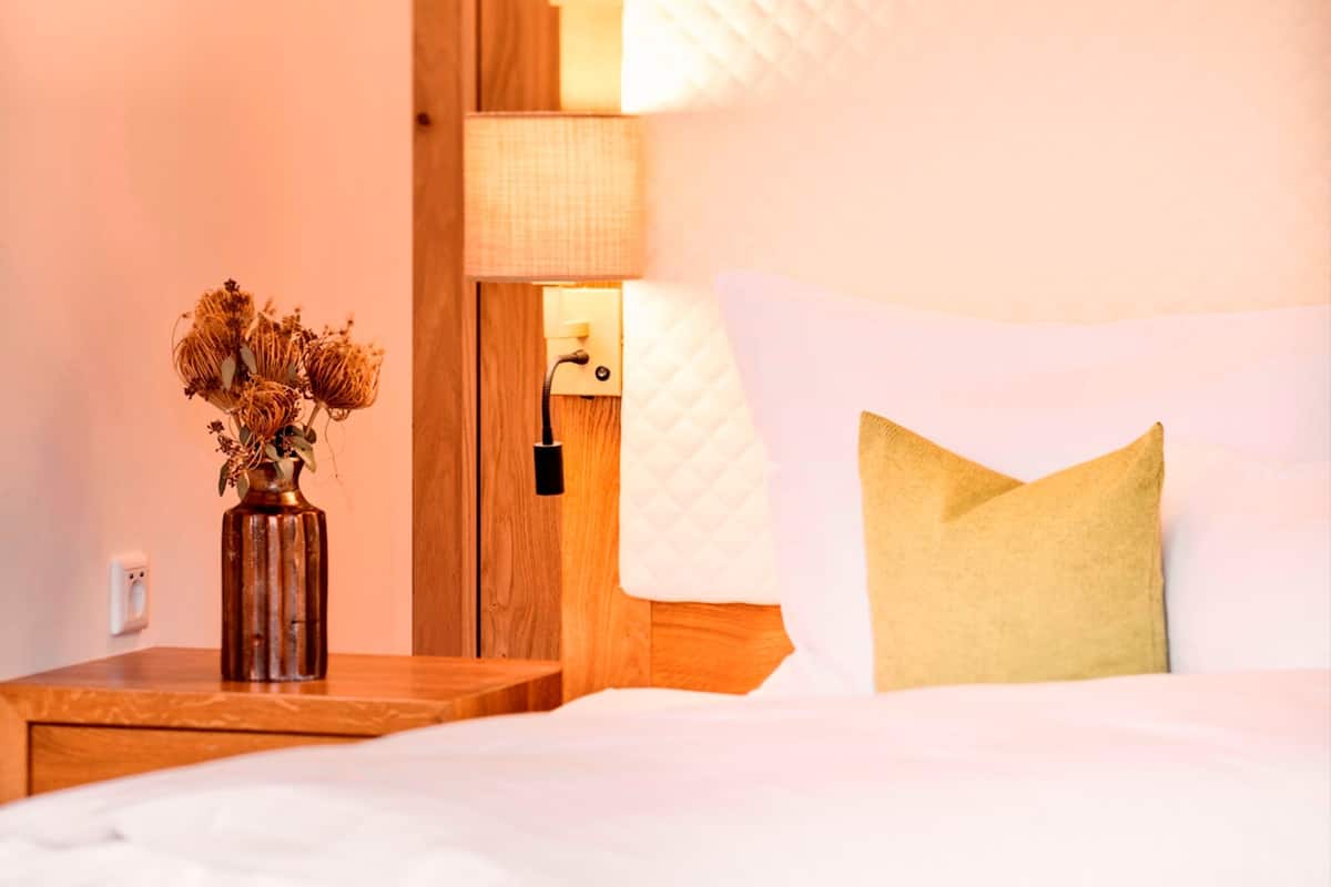 Une chambre à coucher avec une tête de lit en bois, une table de chevet avec une lampe et un vase contenant des fleurs séchées.
