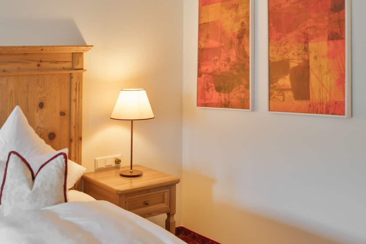 Une chambre d’hôtel avec une tête de lit en bois, une table de chevet avec une lampe, un lit avec une literie blanche et deux tableaux abstraits accrochés au mur.