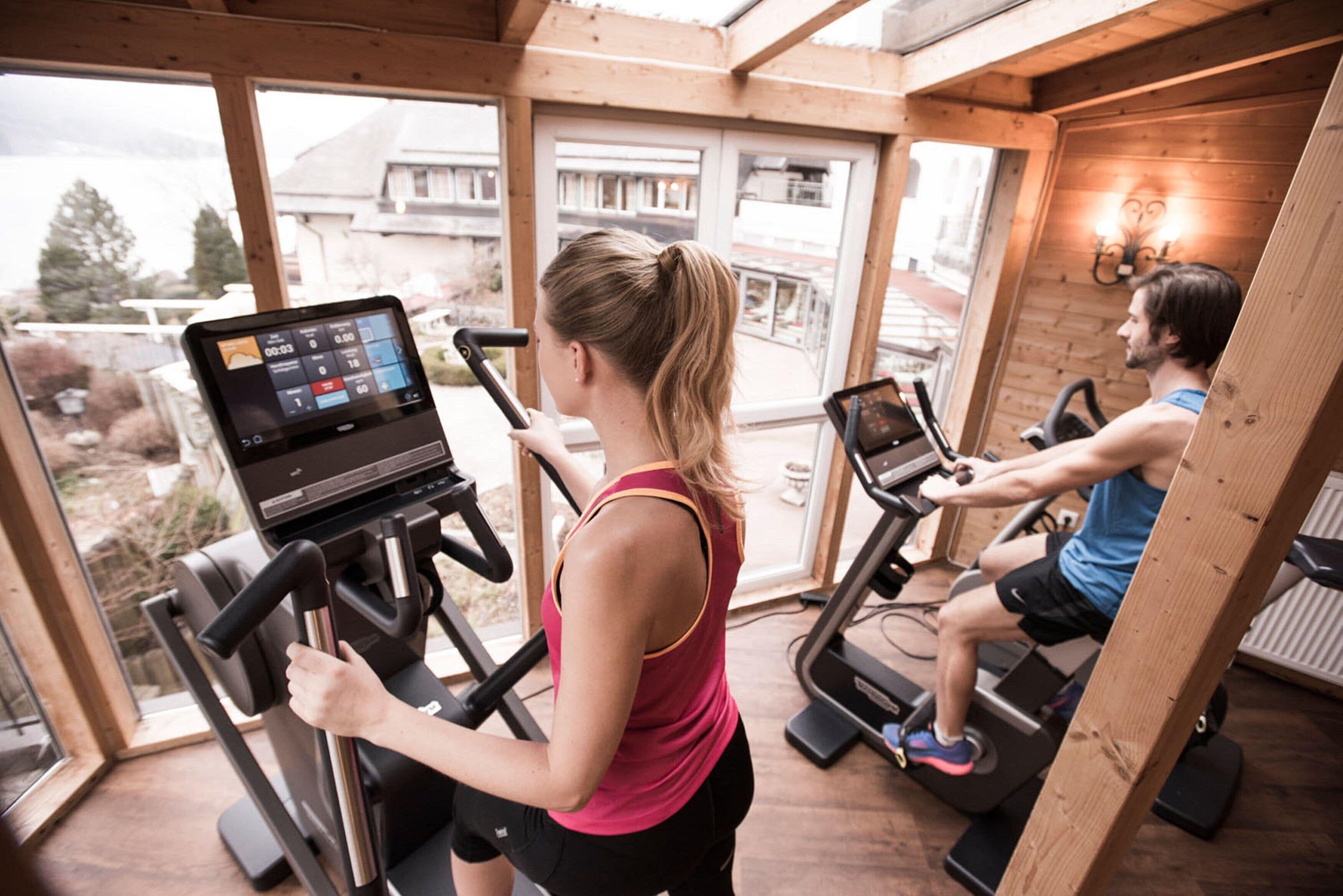Un gimnasio con cintas de correr y una pantalla digital, ventanas amplias y un interior de madera.