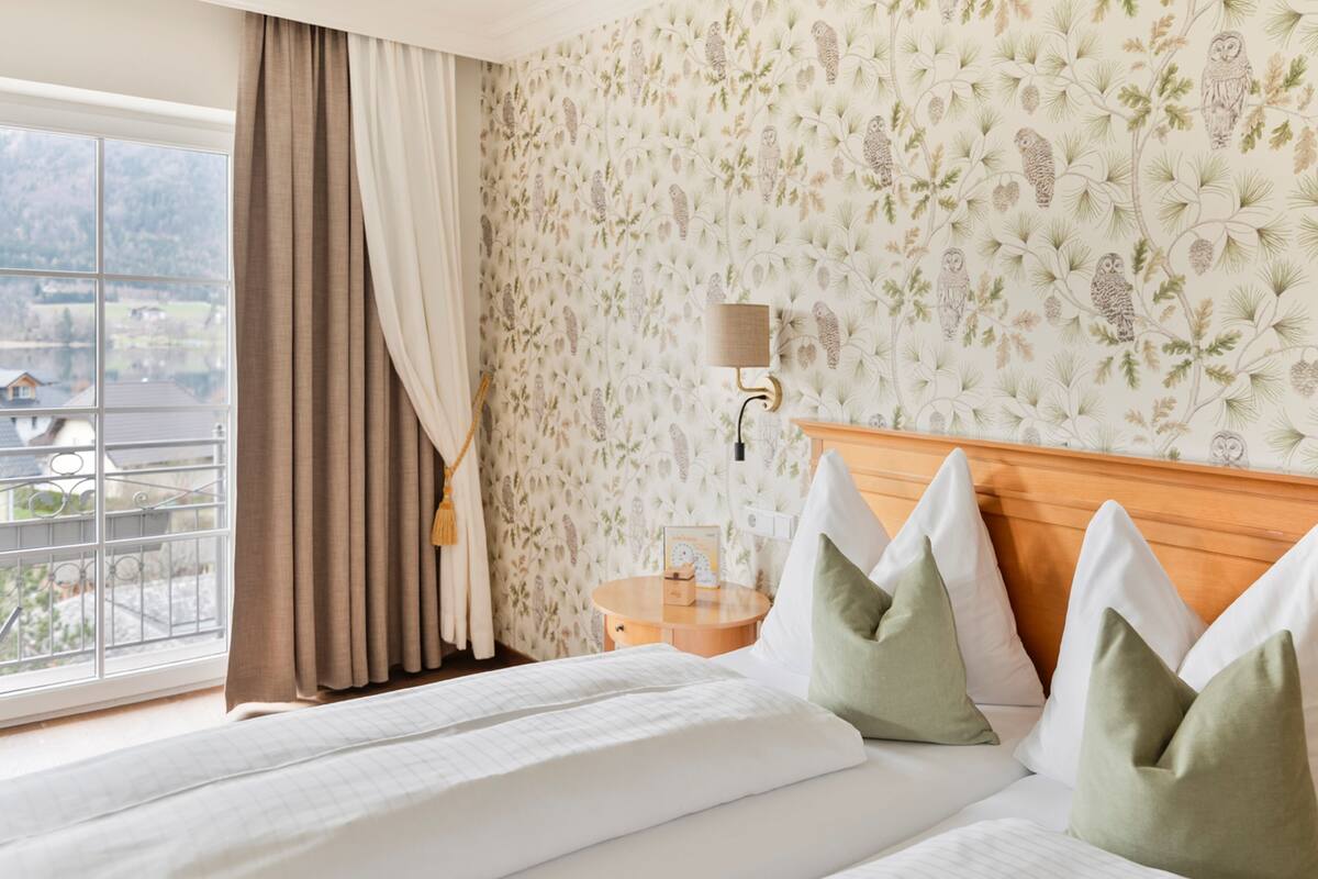 Une chambre d’hôtel avec un lit, une table de chevet, une lampe et une fenêtre avec des rideaux.