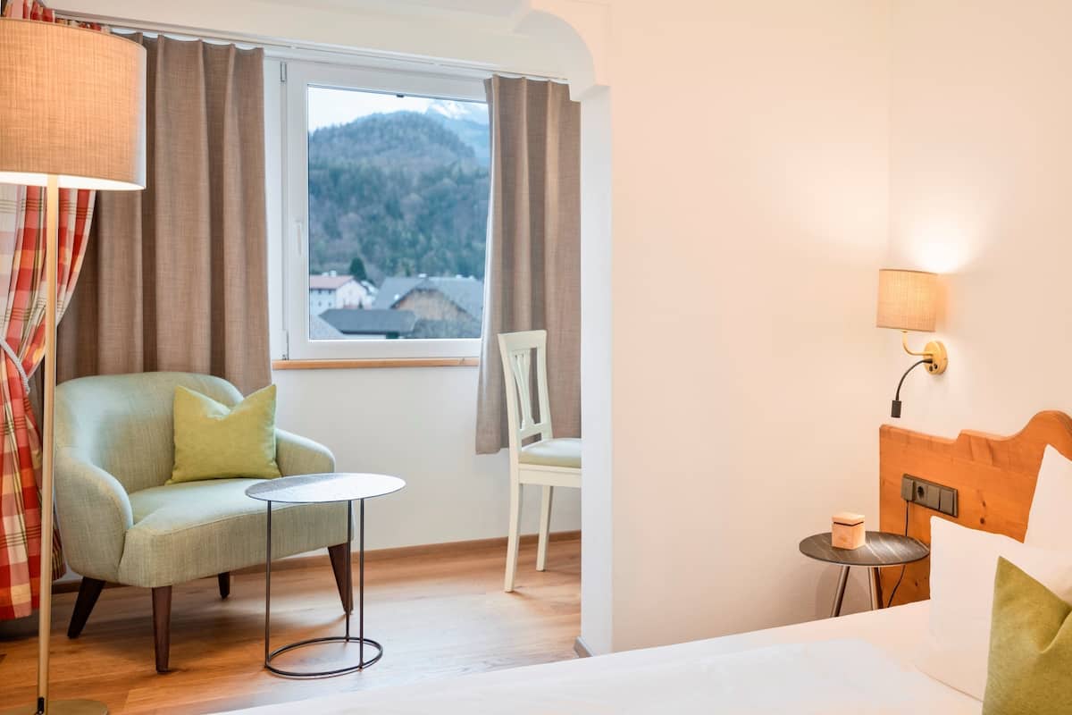 Une chambre d’hôtel avec un lit, une petite table, une chaise et une vue sur une montagne par la fenêtre.