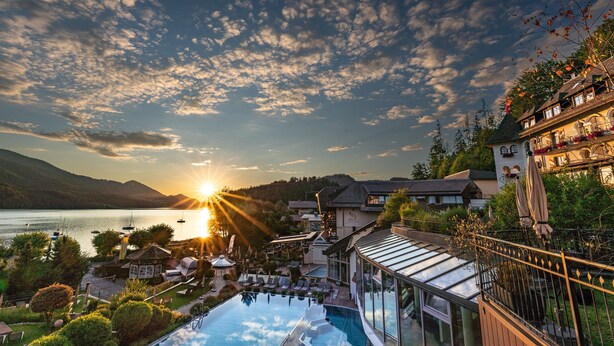 Un resort con piscina, vistas al lago y un atardecer.