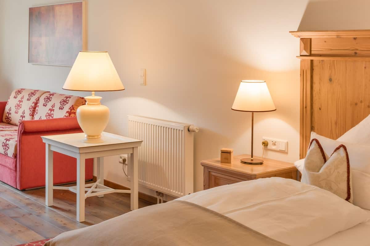 Une chambre d’hôtel avec un lit, une table avec une lampe, un canapé rouge et un meuble en bois.