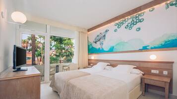Habitación de hotel con dos camas, televisión, escritorio y un ventanal con vistas a palmeras.