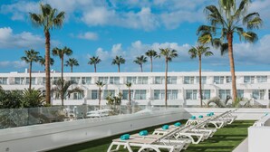 A rooftop pool area with sun loungers, palm trees, and a modern building in the background. - Iberostar Waves Las Dalias -All Inclusive (Adeje)