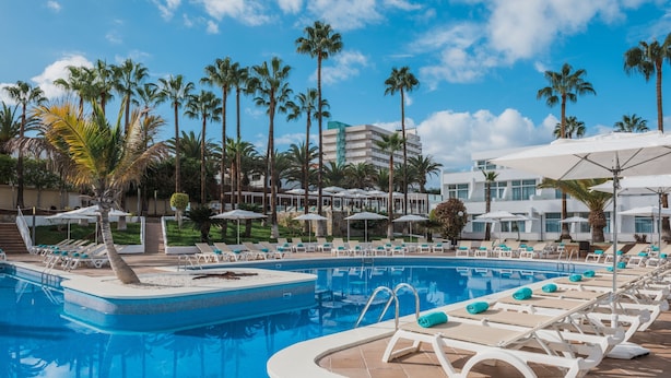 A pool area with lounge chairs, palm trees, and a building in the background. - Iberostar Waves Las Dalias -All Inclusive (Adeje)