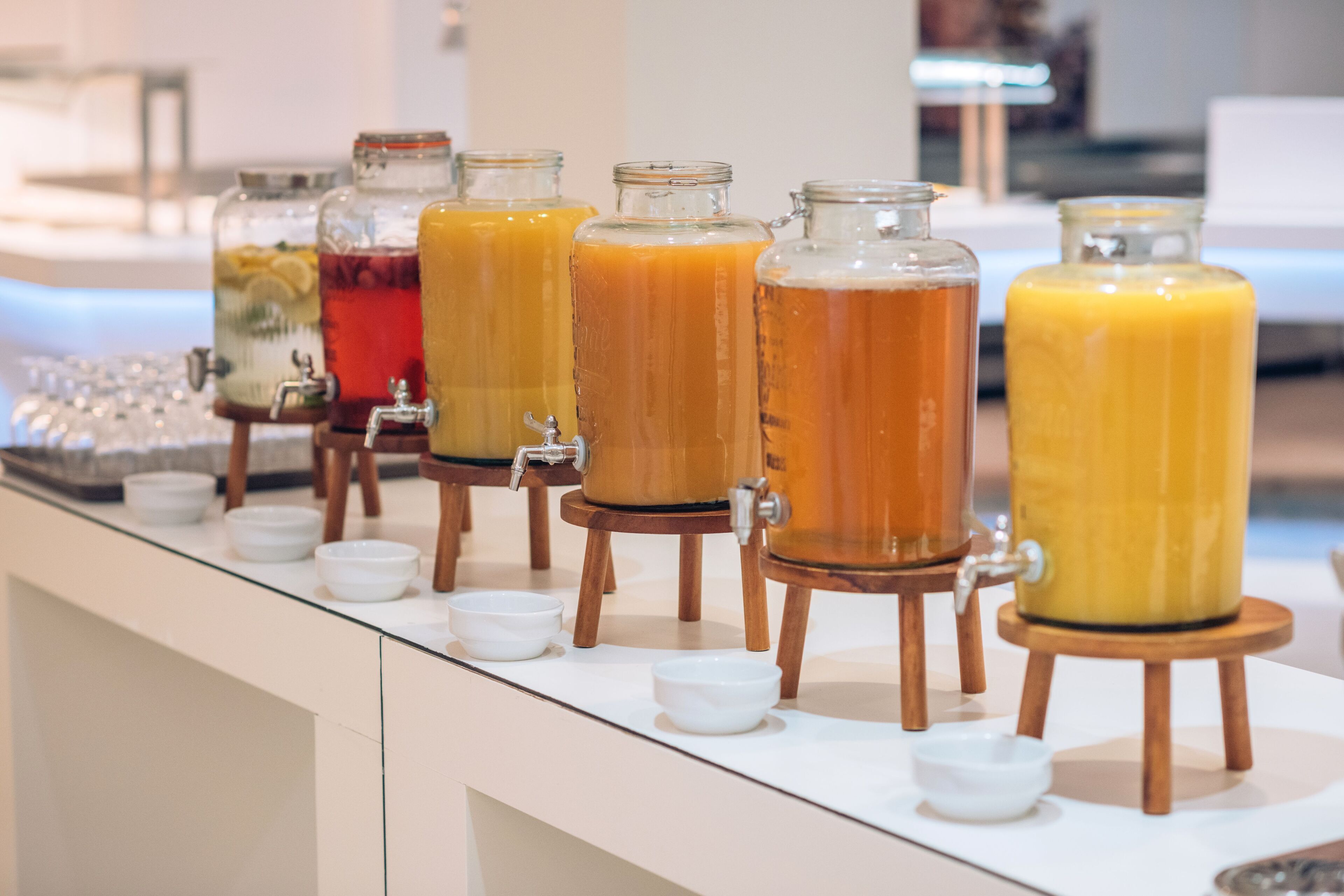 A beverage station with multiple dispensers on wooden stands, each with a tap and a small bowl in front.