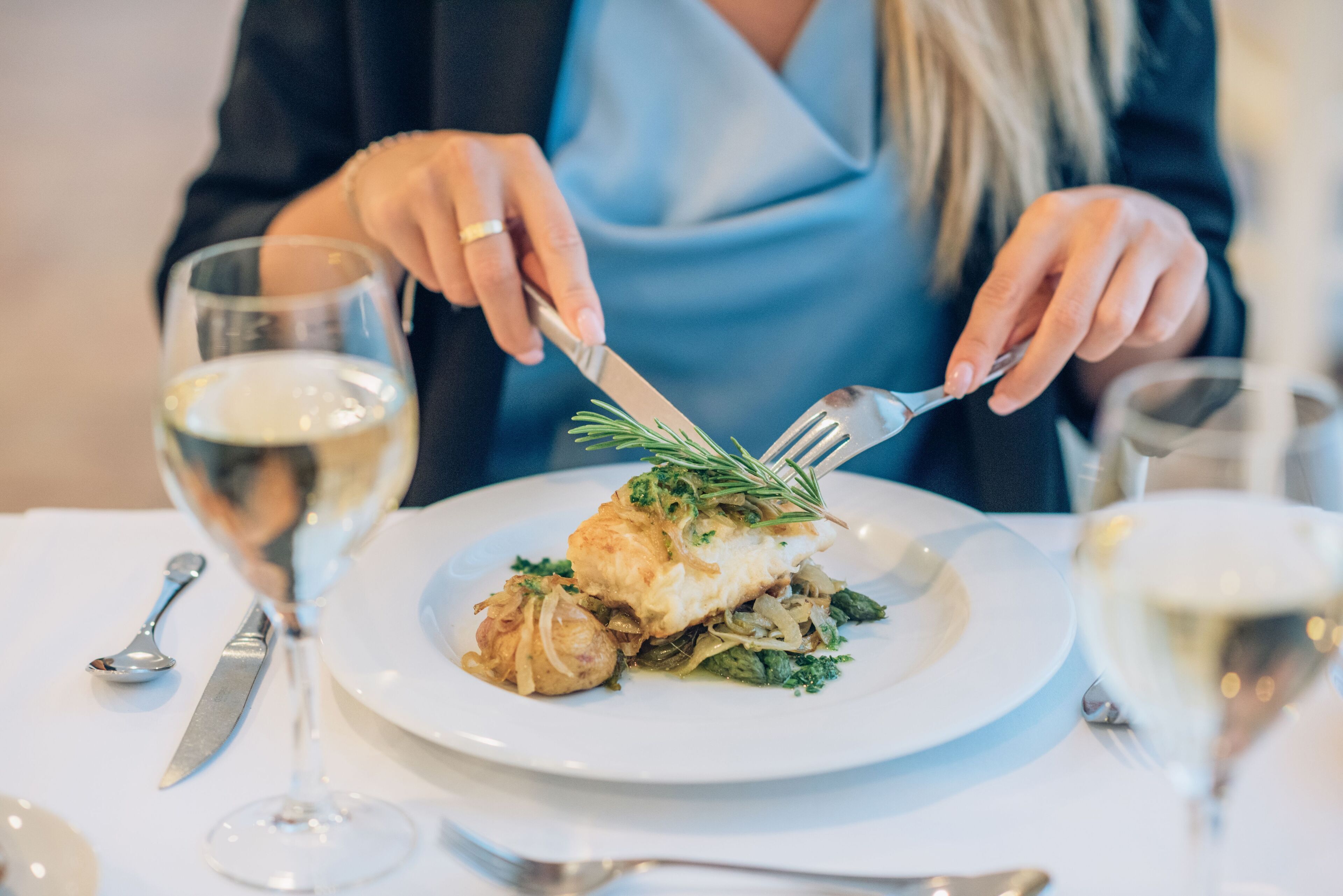 Una persona comiendo en una mesa, con un plato blanco de comida, un tenedor y un cuchillo.