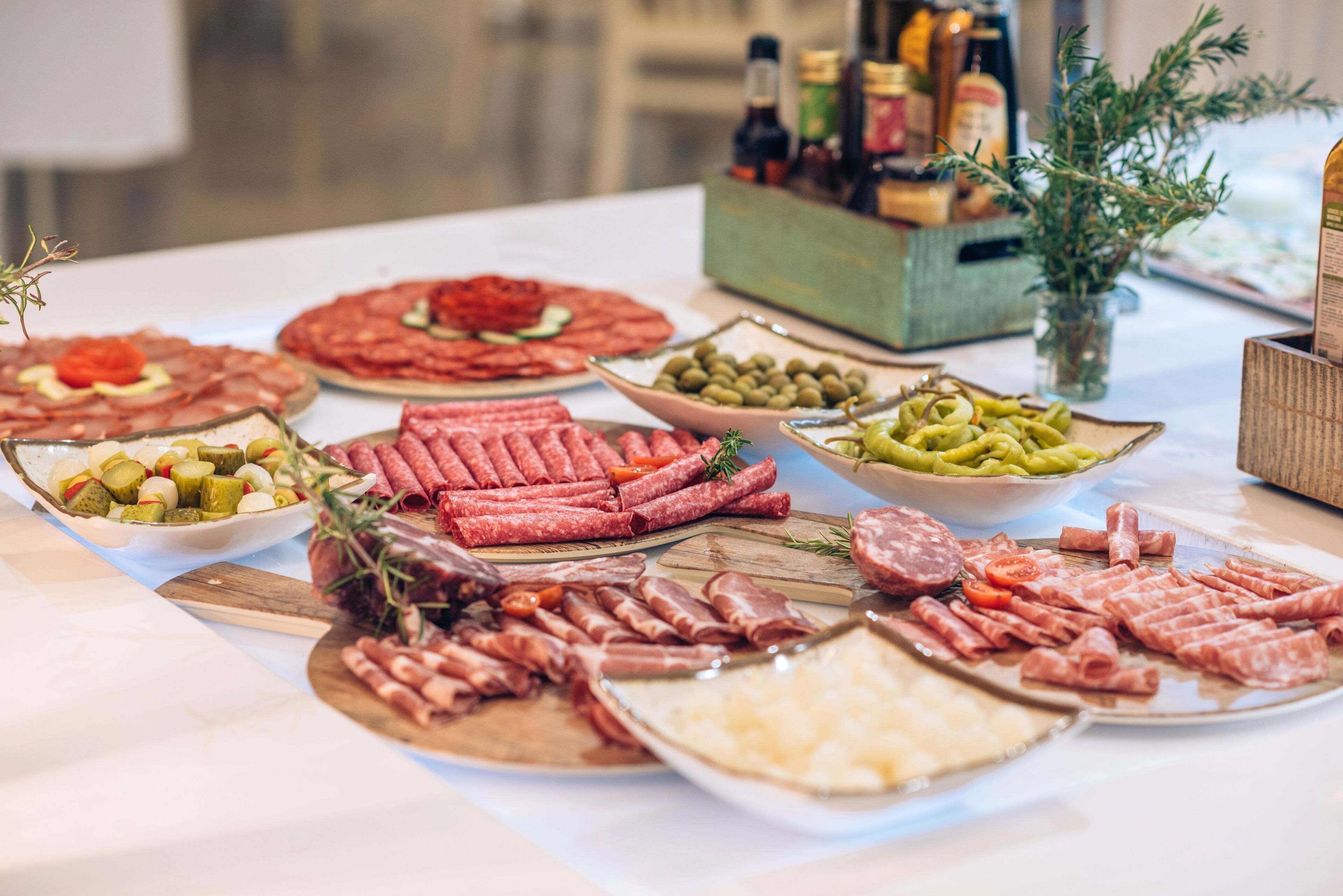 Una mesa con varios tipos de embutidos y quesos, acompañada de aceitunas y pepinillos.