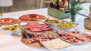 Una mesa con varios tipos de embutidos y quesos, acompañada de aceitunas y pepinillos.