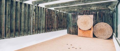 Un espacio interior arenoso con vigas de madera, dos esteras tejidas y varios objetos pequeños esféricos.