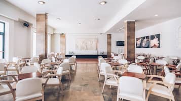 A spacious conference room with white chairs and tables, a stage with a podium, and a large wall art piece.