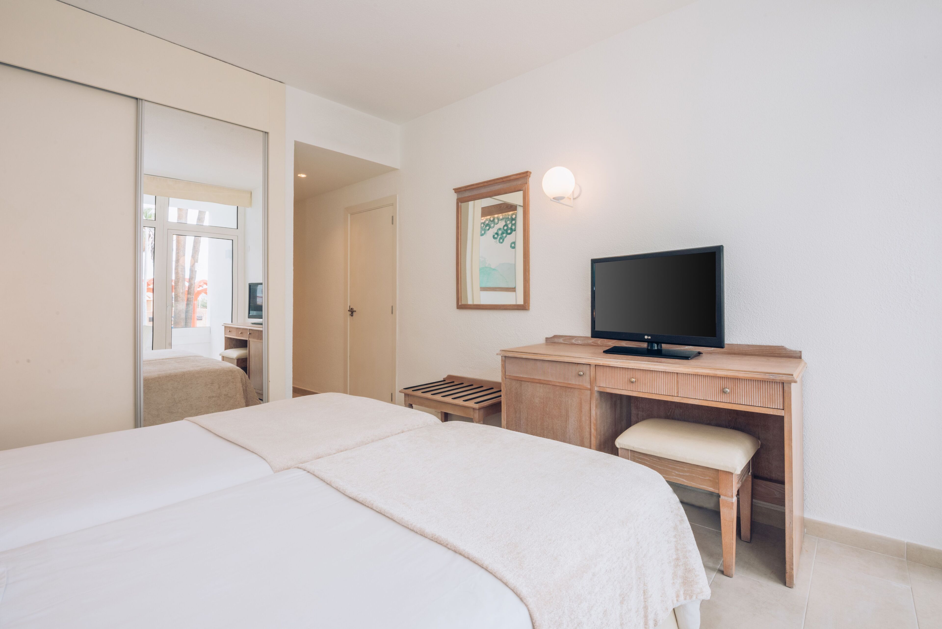 Une chambre d’hôtel avec un lit, un bureau avec une télévision, un petit tabouret et une porte donnant sur une autre pièce.