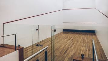 Una cancha de squash con paredes de vidrio, suelo de madera y barandillas metálicas.
