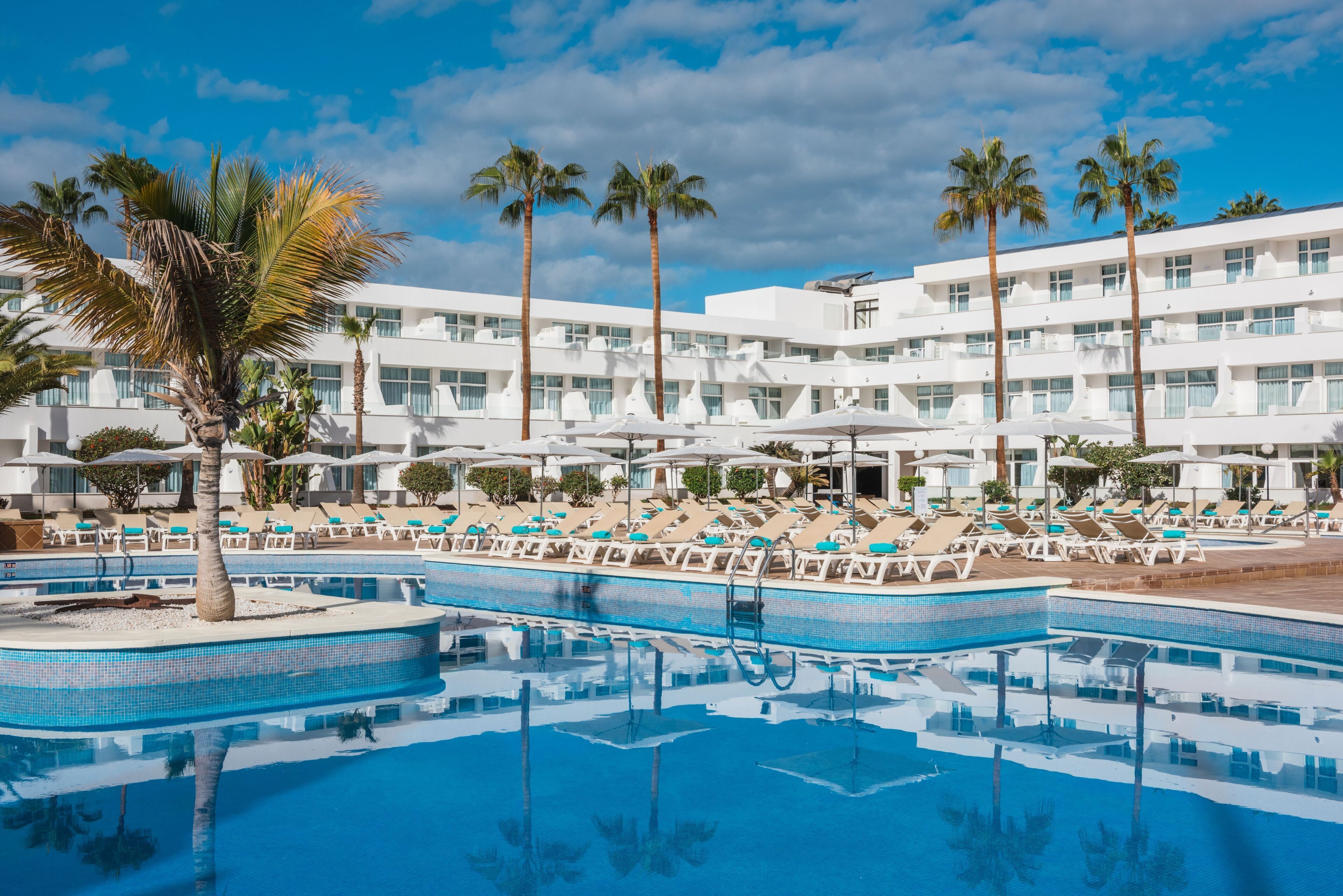 A hotel with a pool area, multiple lounge chairs, and palm trees.