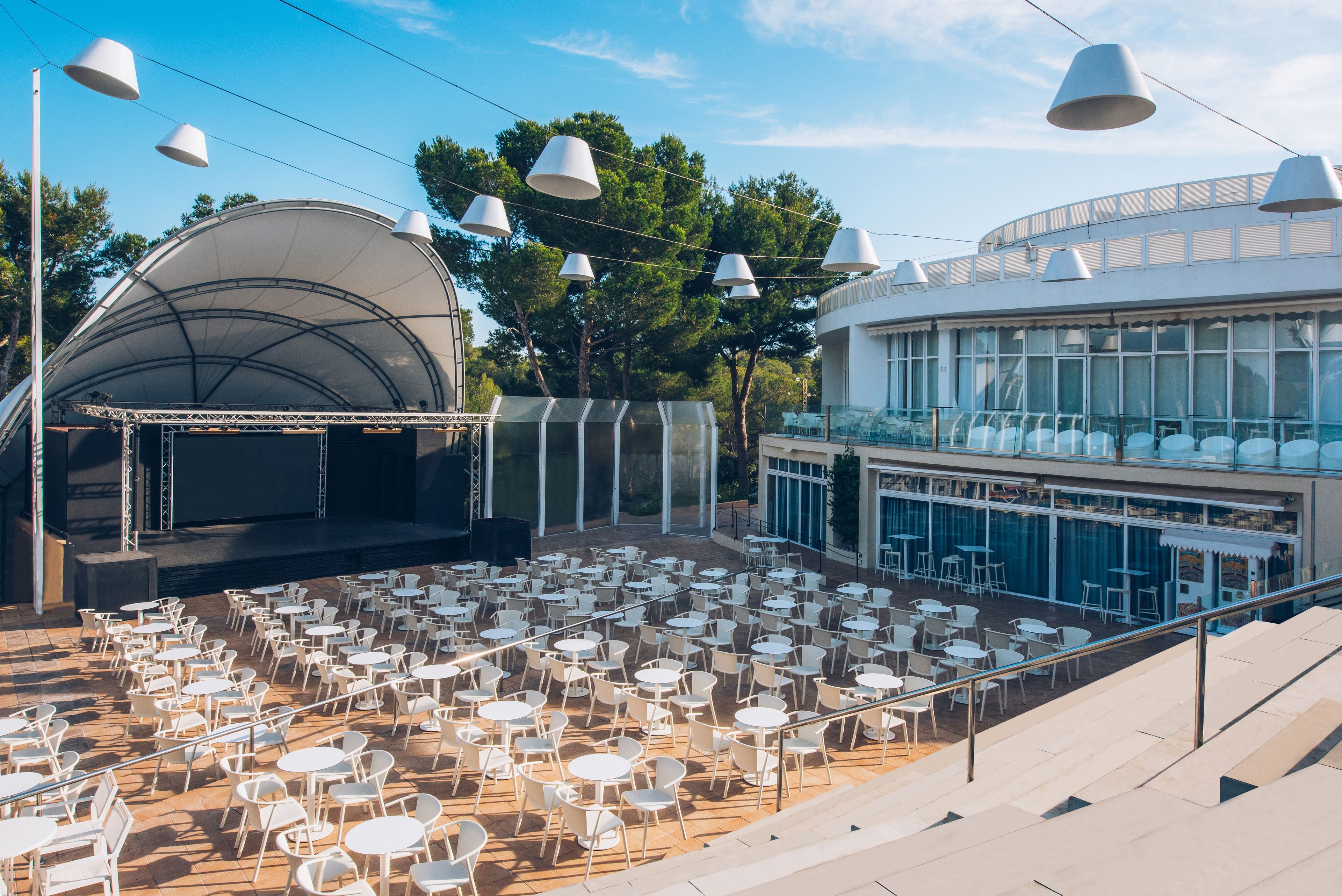 An outdoor seating area with multiple tables and chairs, a stage, and a covered area.
