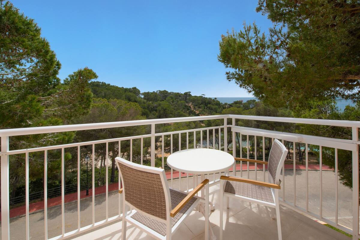 A balcony with white railings, two wicker chairs, and a small round table.