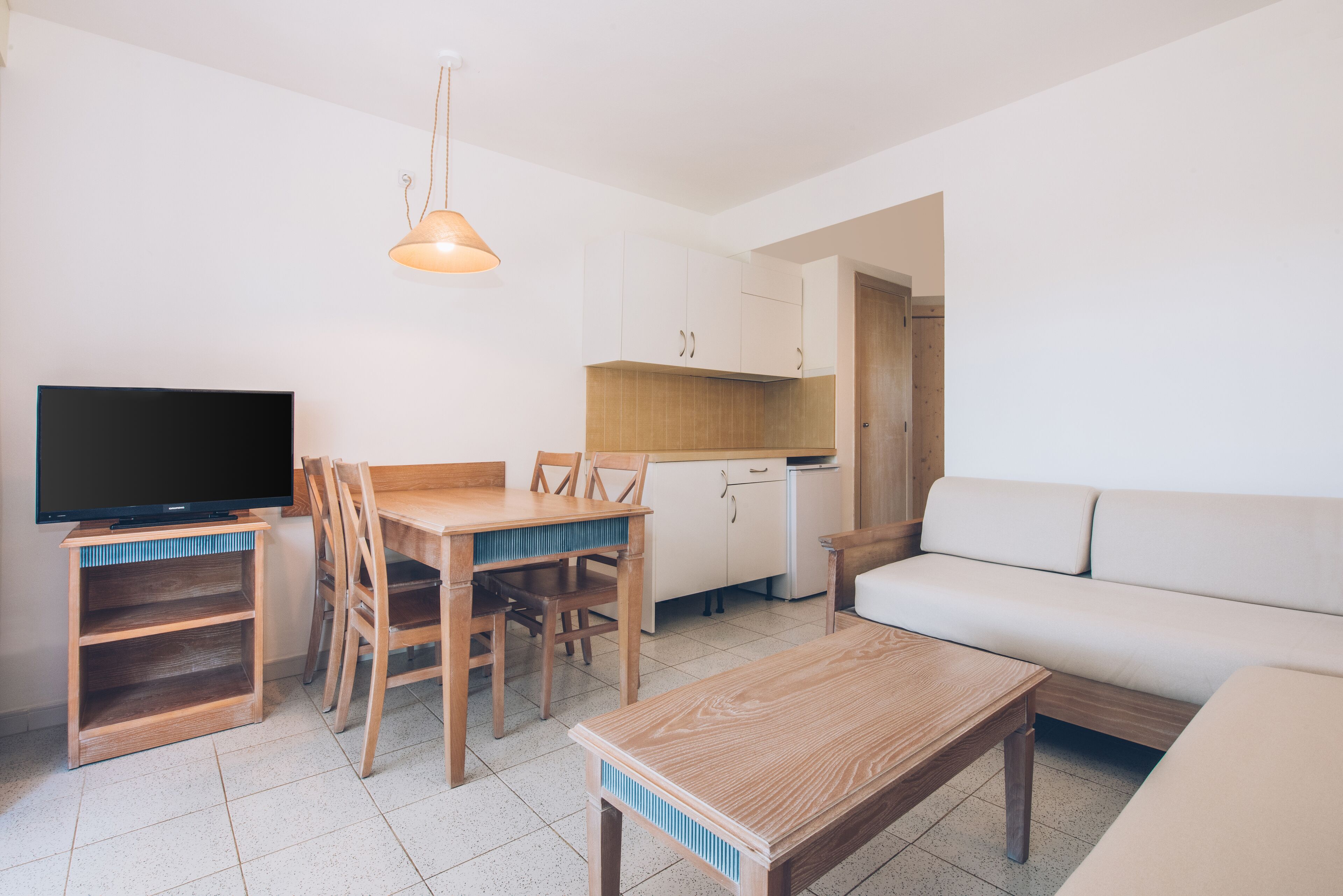 A compact living space with a dining table, chairs, a sofa, a television, and a kitchenette.